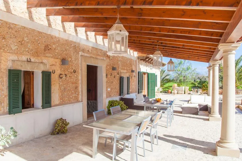 A covered outdoor dining terrace with a long table and seating beside the house.