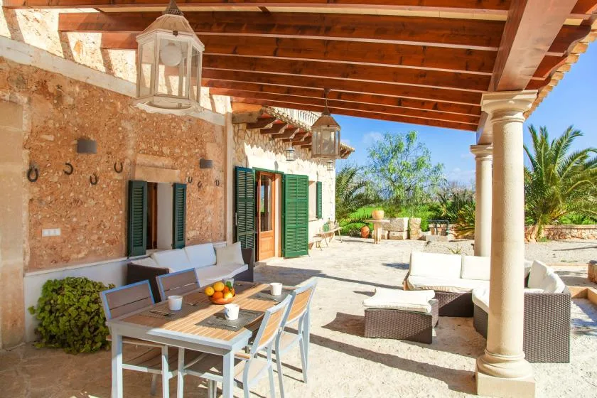A covered outdoor patio with a dining table and seating overlooks a sunny garden.