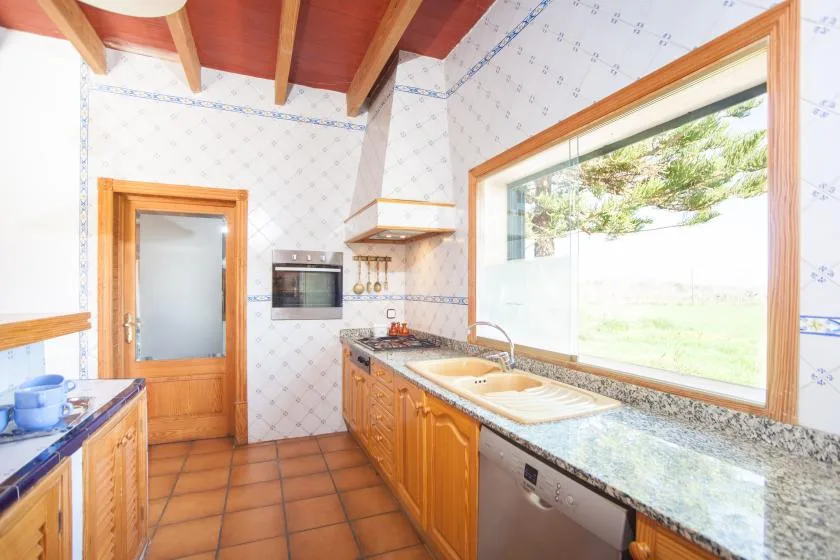 A tiled kitchen with wooden cabinets, a sink, and a large window.