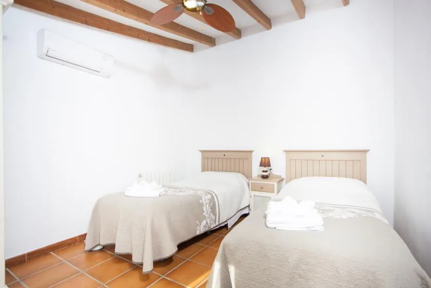 A bright bedroom with two beds, a small bedside table, and exposed ceiling beams.