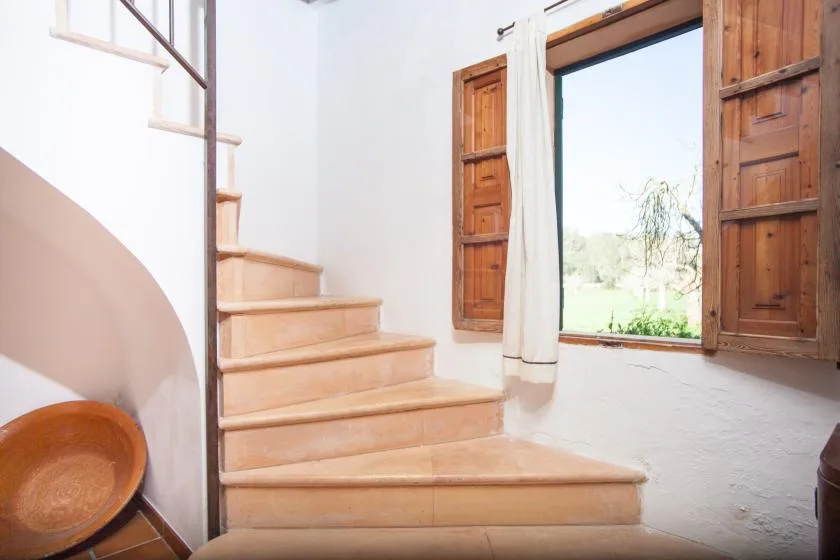 A curved staircase leads up beside an open window with wooden shutters.