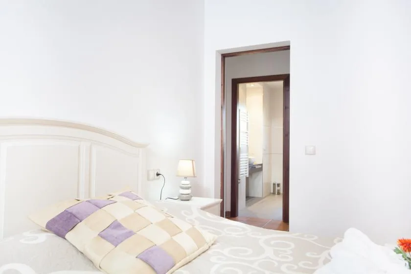 A bedroom with a bed and an open doorway leading to a bright adjoining room.