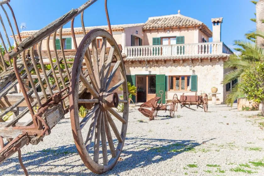 A sunlit courtyard with a rustic wooden cart in front of a stone building.