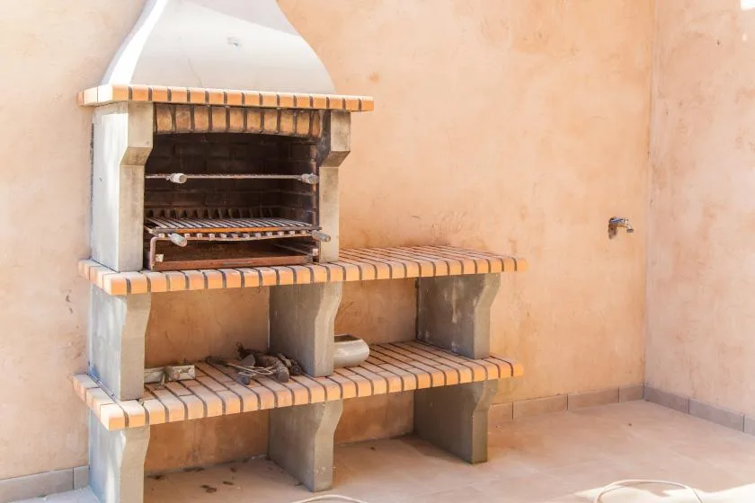 An outdoor brick barbecue built into a stucco wall.