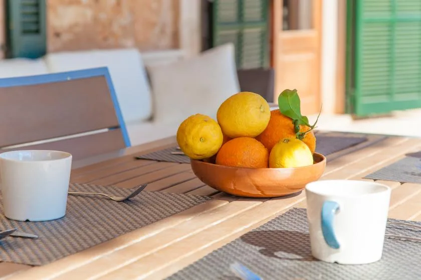 A dining table holds a bowl of citrus fruit beside two mugs.