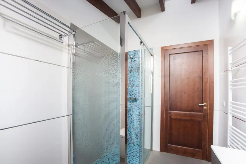 A tiled bathroom with a glass shower and a wooden door.