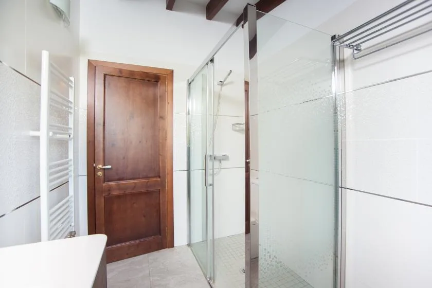 A tiled bathroom with a glass shower and wooden door.