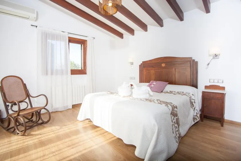 A bright bedroom with a wooden bed, white bedding, and exposed ceiling beams.