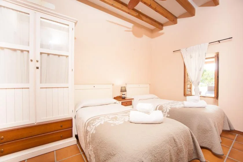 A bedroom with two beds, a curtained window, and exposed ceiling beams.