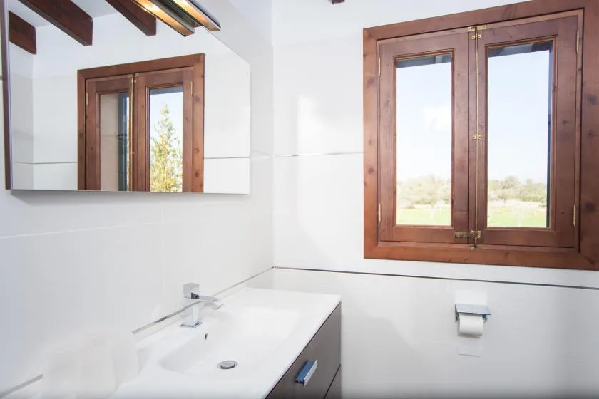 A bright bathroom with a sink beneath a mirror and a wooden-framed window.