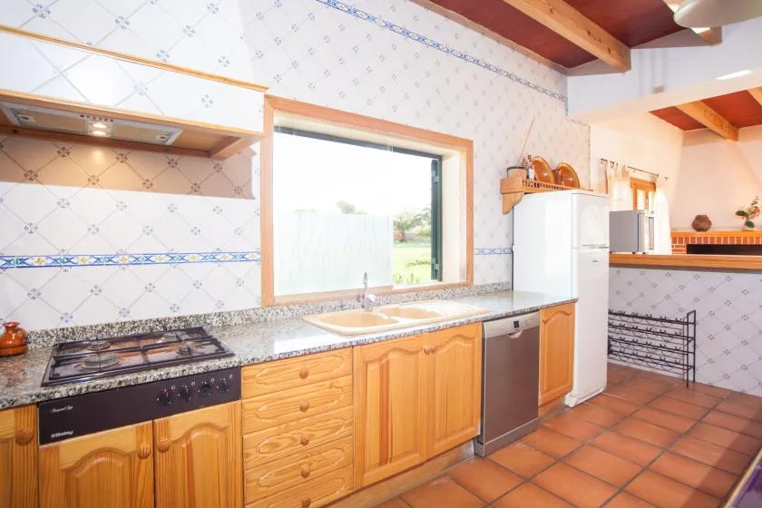 A tiled kitchen with wooden cabinets, a countertop, and a window.