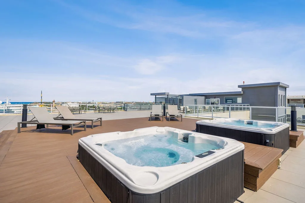The rooftop terrace features hot tubs and loungers overlooking the expansive surrounding area, offering a relaxing space under clear skies.