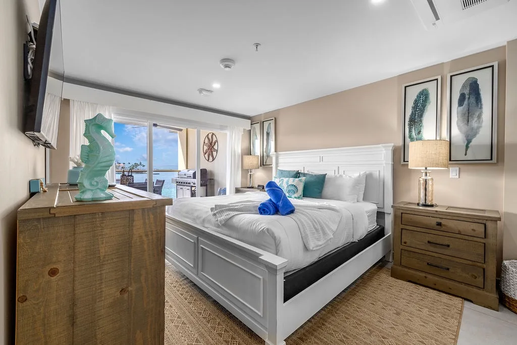 Wake up to stunning water views from your cozy bedroom retreat. The plush king bed, coastal decor, and private balcony access create the perfect escape for relaxation.