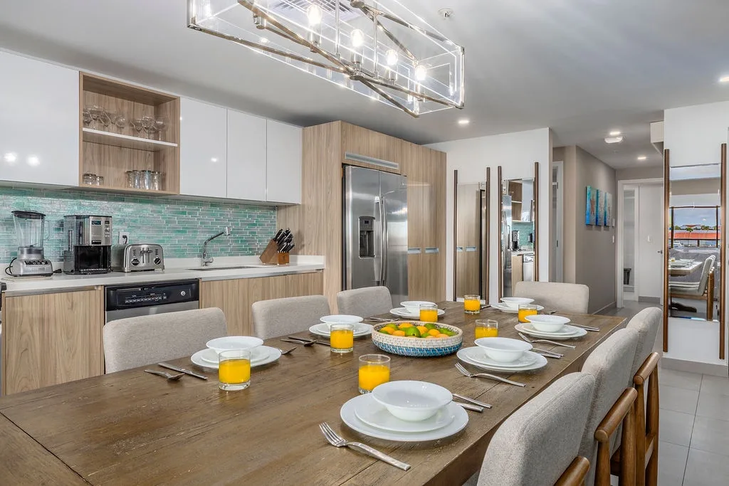 Gather around this spacious dining table, where fresh citrus and morning light set the stage for your shared meals in a sleek, fully equipped kitchen designed for effortless group cooking.