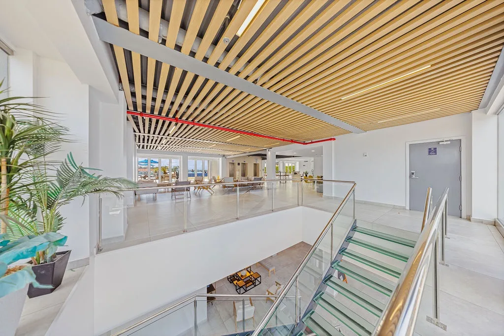 This contemporary two-story lobby features a striking wooden slatted ceiling, modern glass railings, and abundant natural light creating an airy, welcoming first impression.