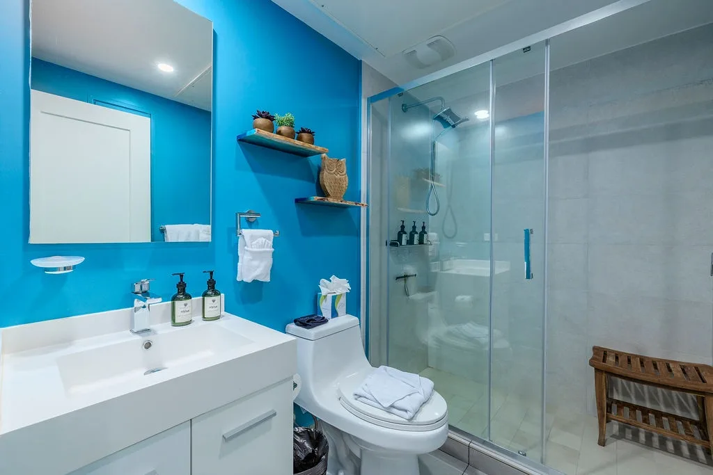 Step into your modern bathroom where vibrant blue walls meet sleek fixtures. Luxurious amenities await, with a spacious glass-enclosed shower and thoughtful touches throughout your private retreat.