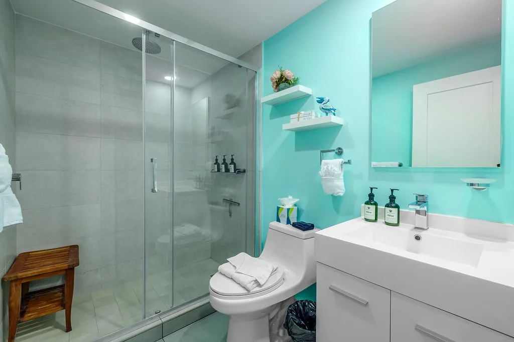Step into your modern bathroom with refreshing turquoise walls, a spacious walk-in shower, and sleek white fixtures. Fresh towels and thoughtful amenities await, making it easy to unwind after exploring.