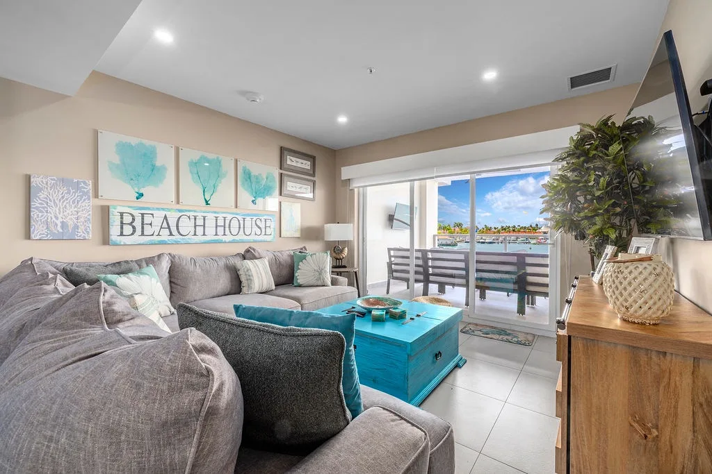 Step into your bright, coastal-inspired living room where plush seating, beachy décor, and open balcony views invite you to unwind in style and comfort.