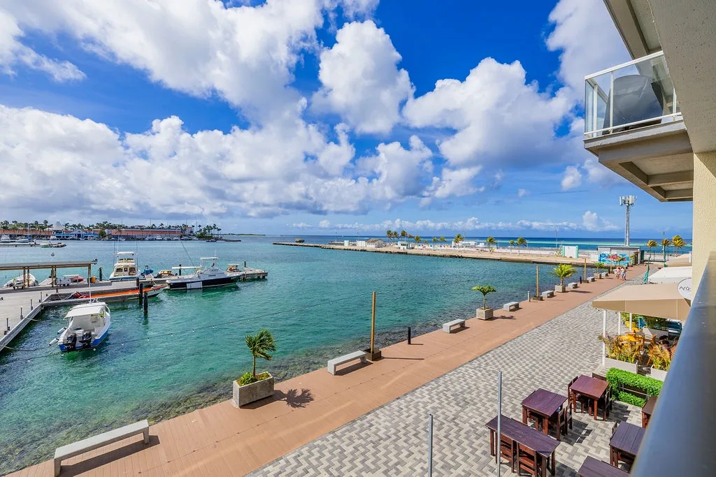 Coastal property with marina access and waterfront promenade overlooking turquoise harbor waters and distant shoreline under dramatic cloud formations.