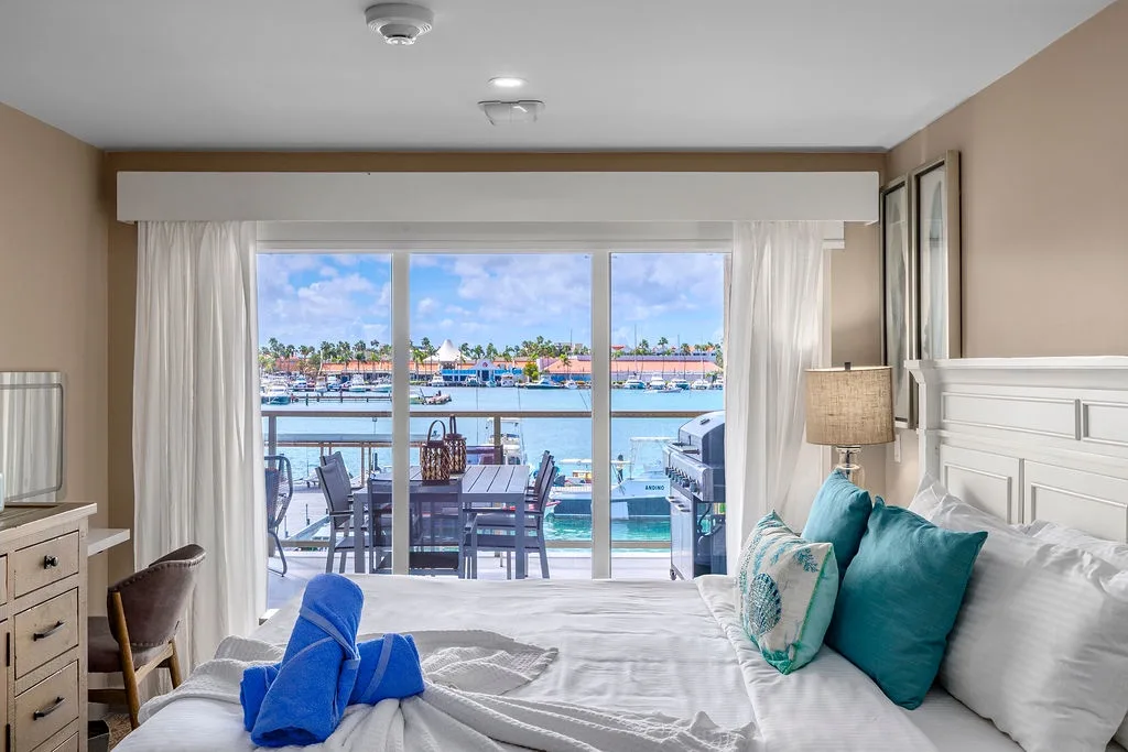 Imagine waking up to sparkling marina views through your window. Crisp white linens, turquoise accents, and a private balcony await—your waterfront escape.
