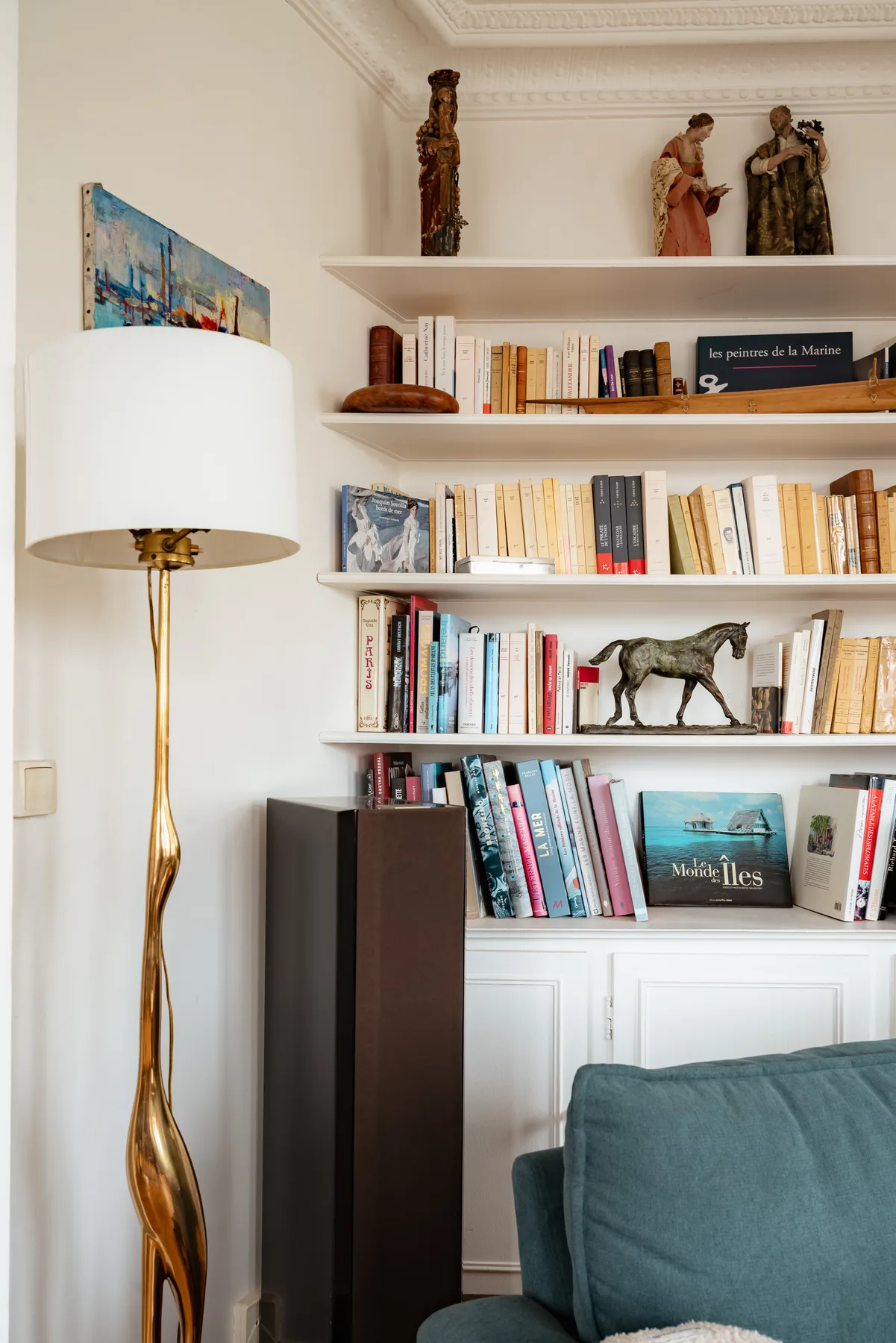A living room bookshelf filled with books and decorative figures beside a floor lamp.