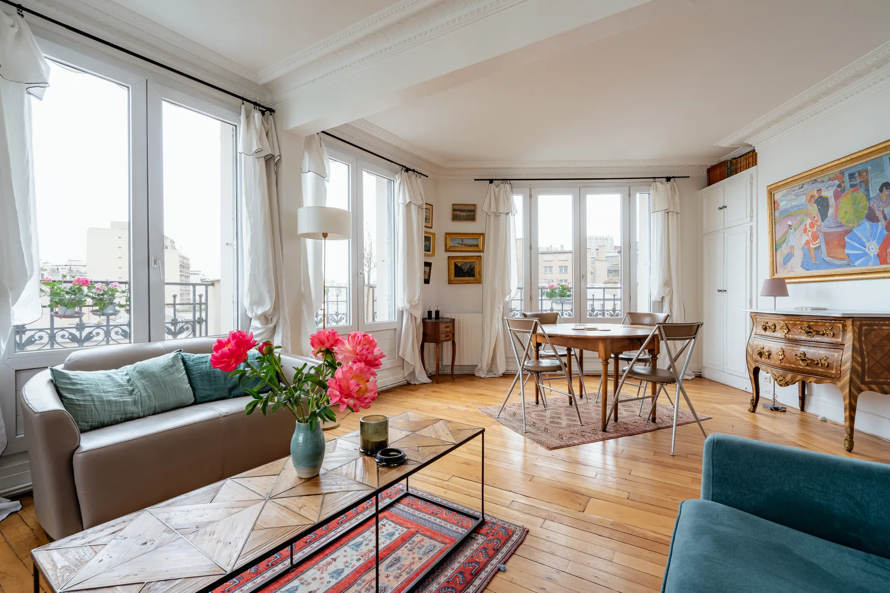 A bright living and dining room has tall windows and seating around a table.