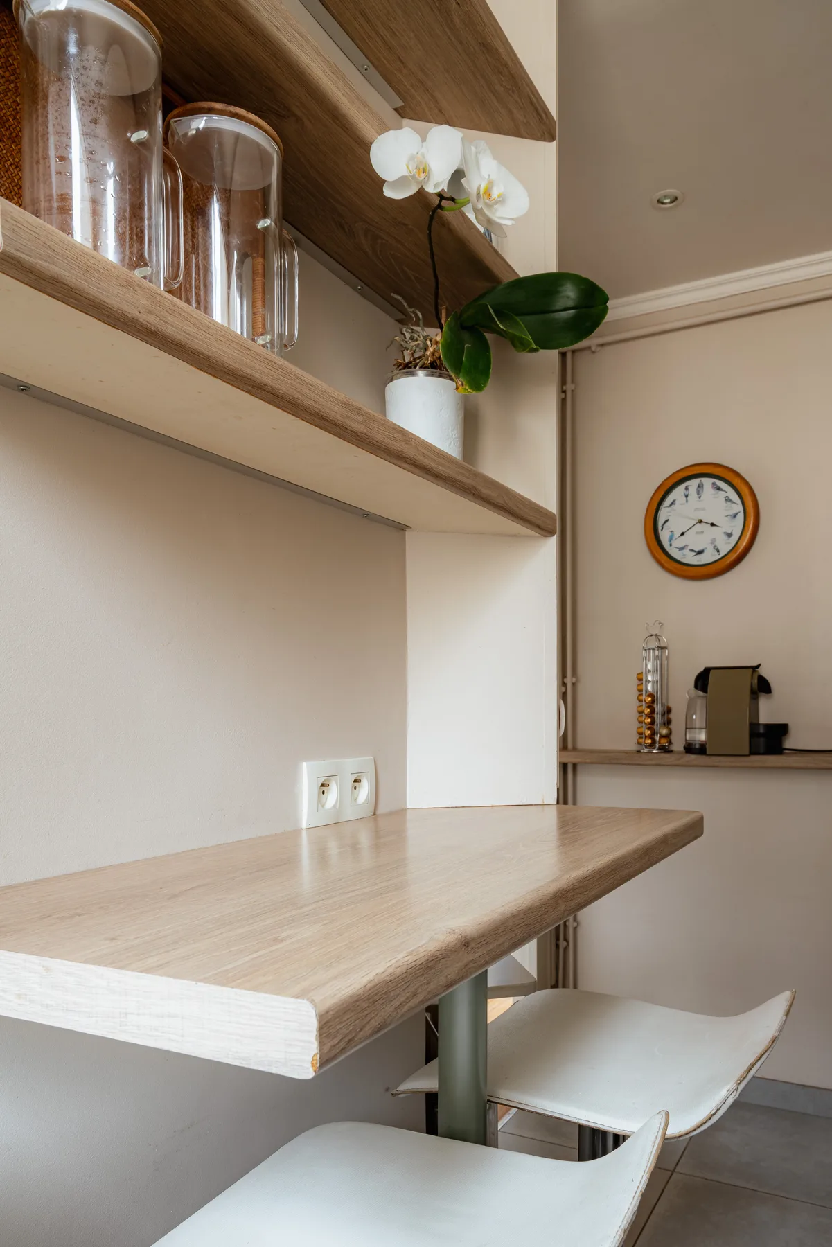 A small dining nook with a wooden counter, seating, and an orchid on a shelf.