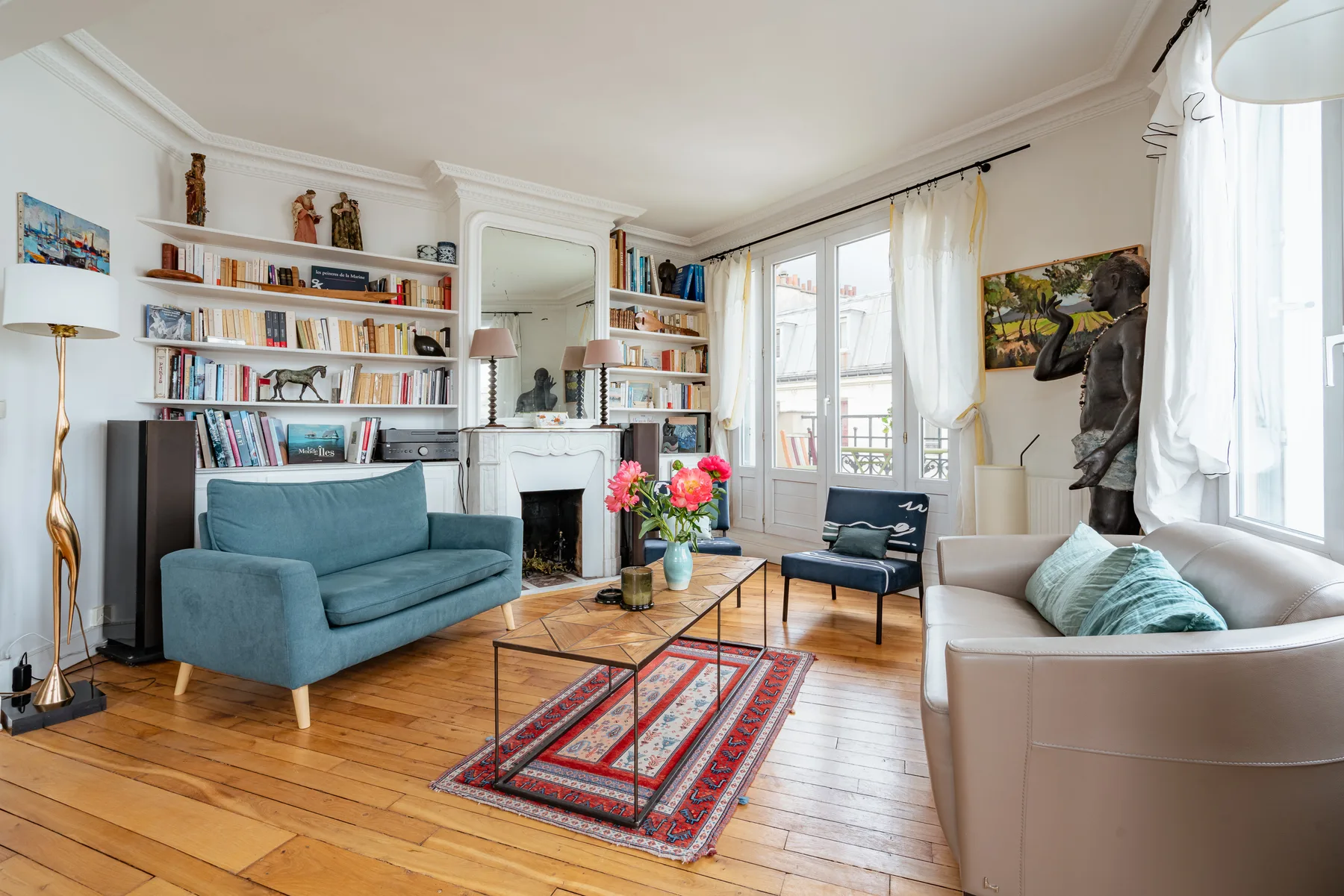 A bright living room with seating, bookshelves, and tall windows.