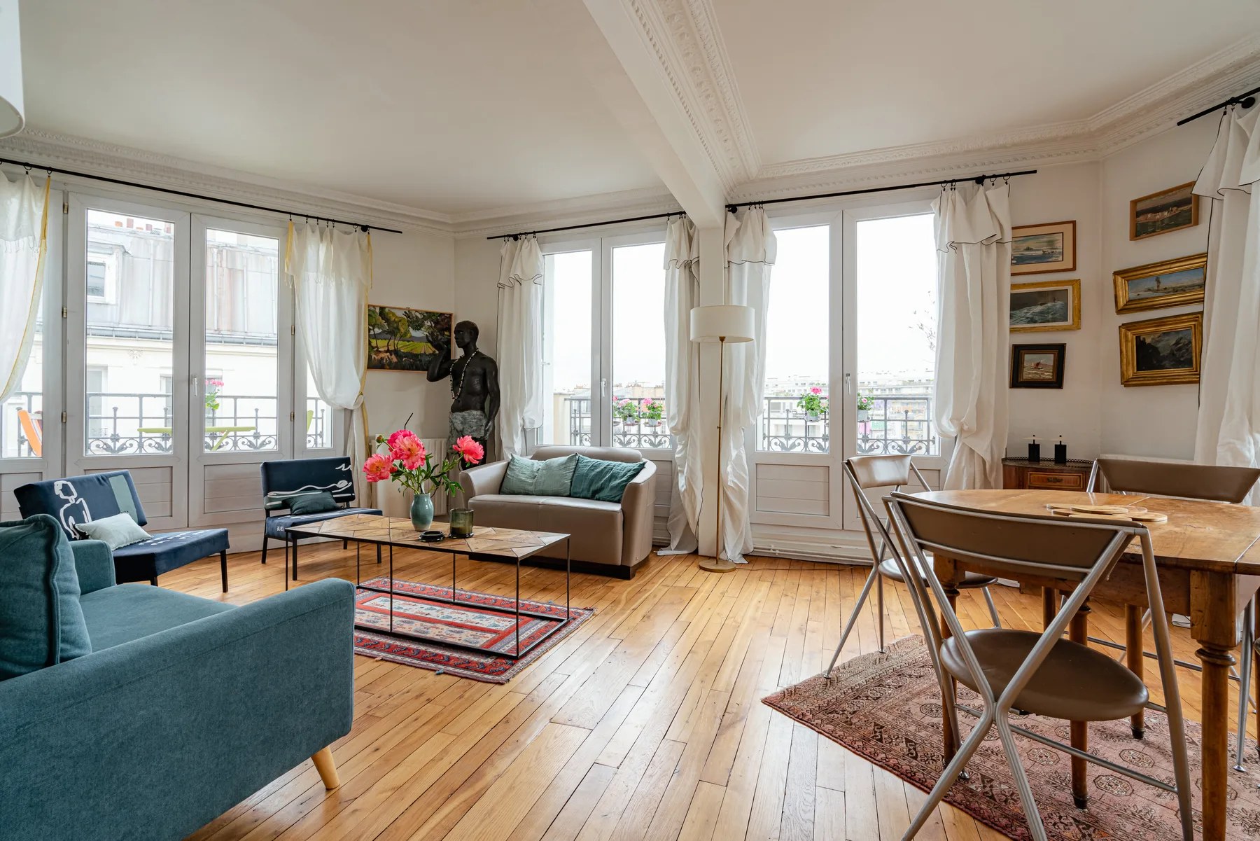 A bright living and dining room with large windows and seating around a coffee table.