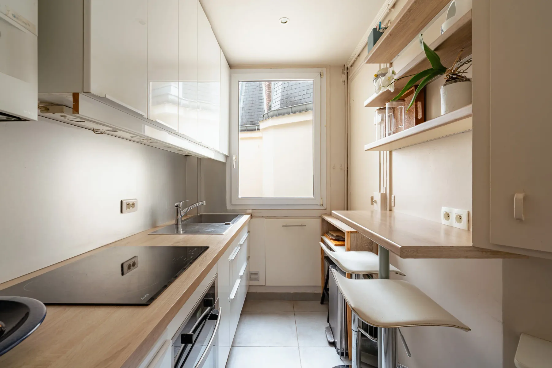 A narrow kitchen with a cooktop, sink, and counter seating.