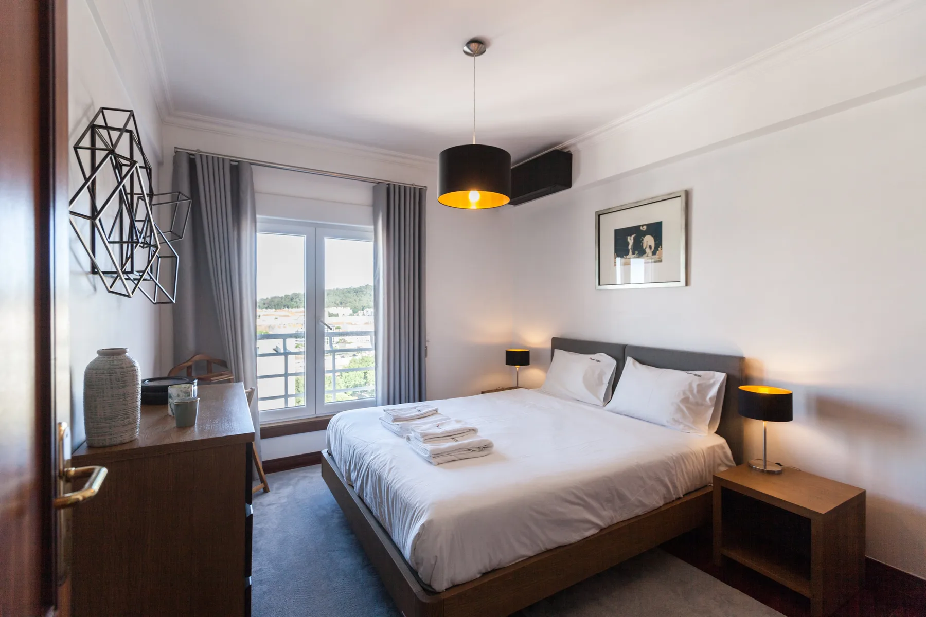 Un dormitorio luminoso con cama doble, mesillas y una ventana con balcón.