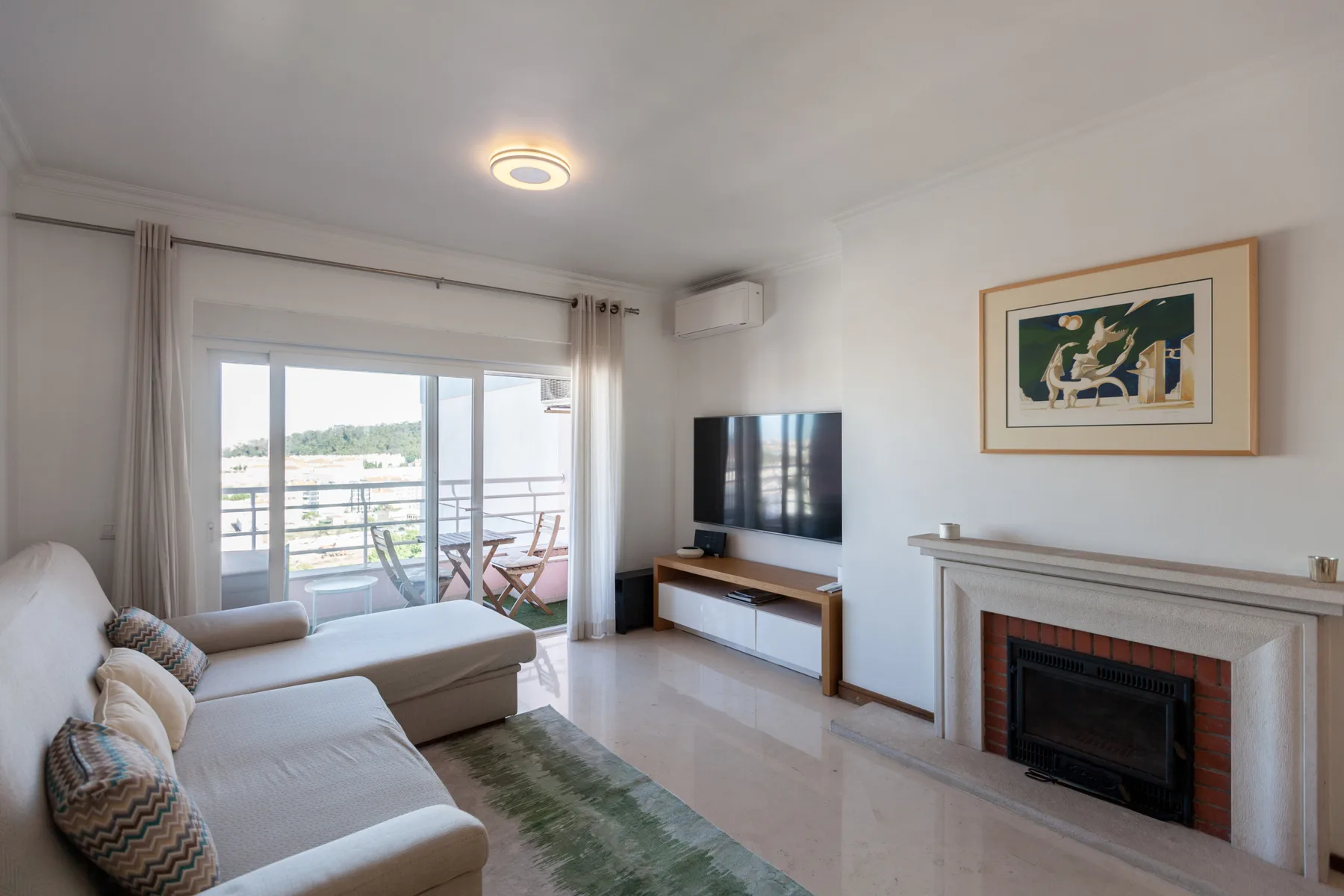 Sala de estar con asientos, televisor y puertas corredizas de vidrio que dan a un balcón.