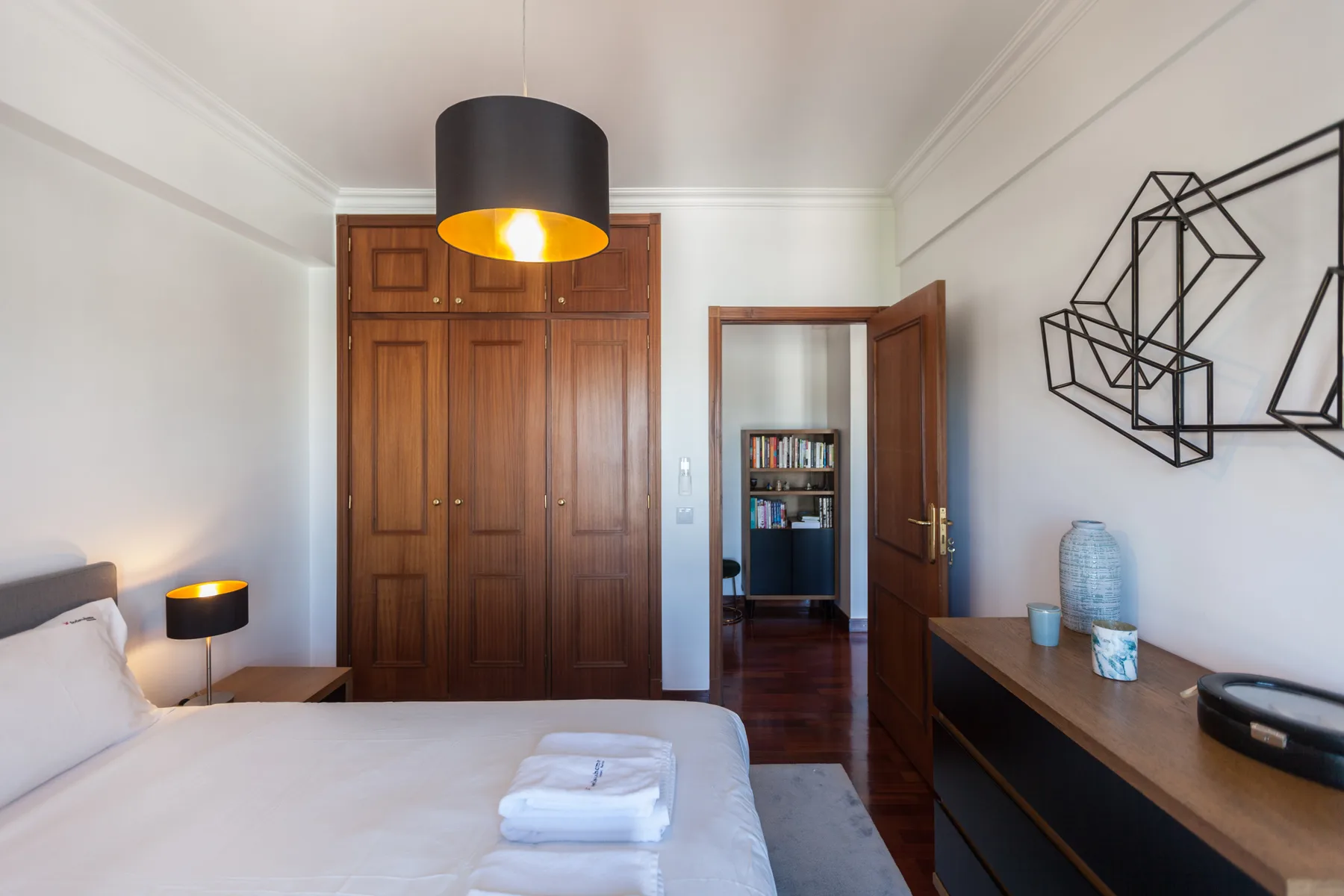Un dormitorio con una cama, un armario de madera y una puerta abierta a otra habitación.