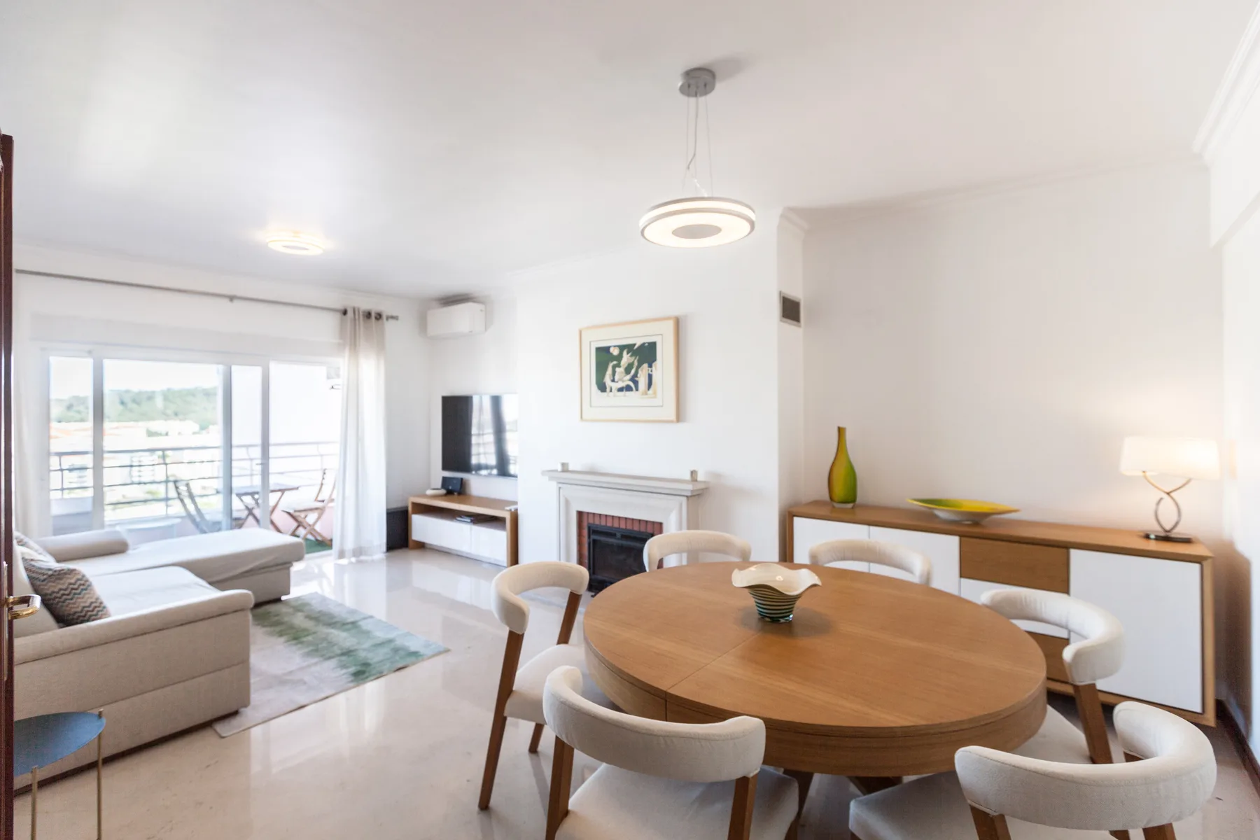 Una luminosa sala de estar y comedor con asientos, un televisor y una mesa redonda.
