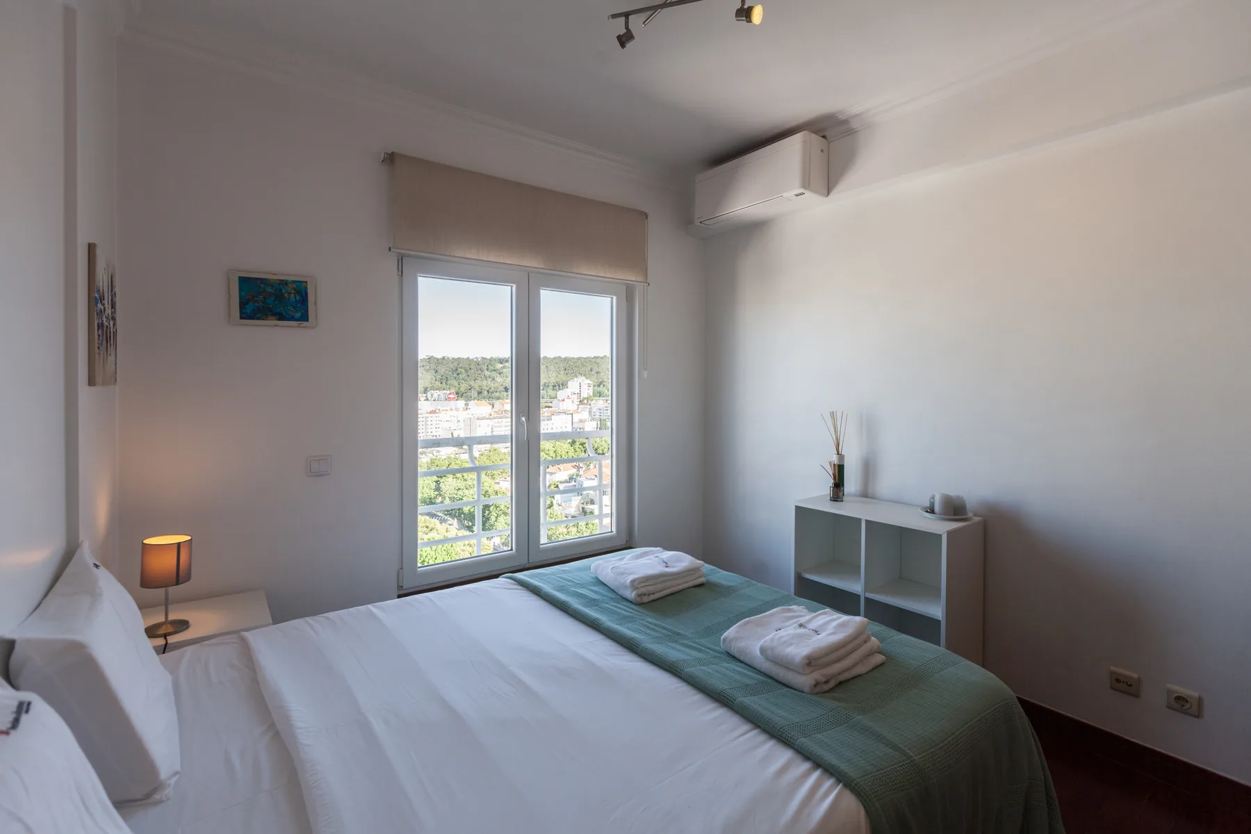 Un dormitorio con una cama, toallas dobladas y una ventana con vistas a la ciudad.