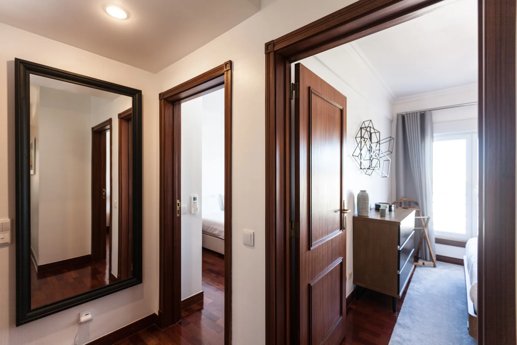 Un pasillo con puertas de madera oscura da a una habitación luminosa con escritorio.