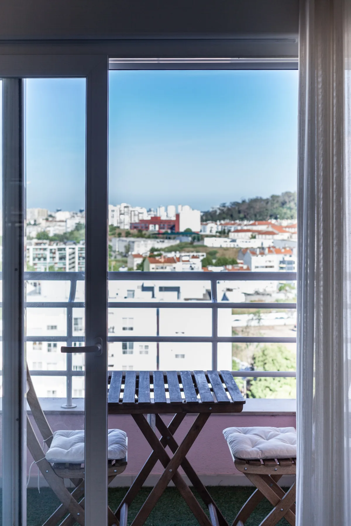 Un balcón con una mesa pequeña y asientos ofrece vistas a los edificios cercanos.