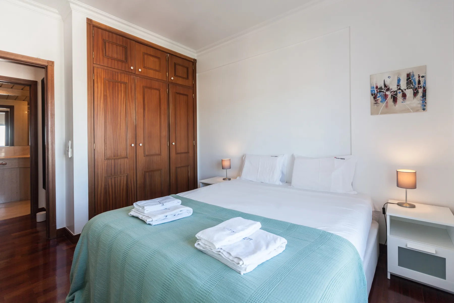 Un dormitorio con una cama bien tendida, toallas dobladas y armarios de madera.