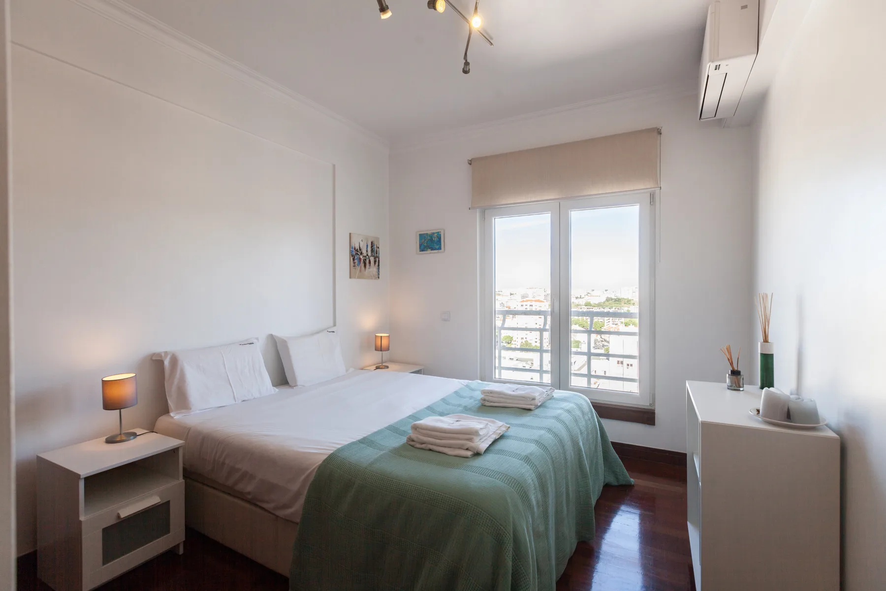 Un dormitorio luminoso con una cama vestida de blanco y una colcha verde.