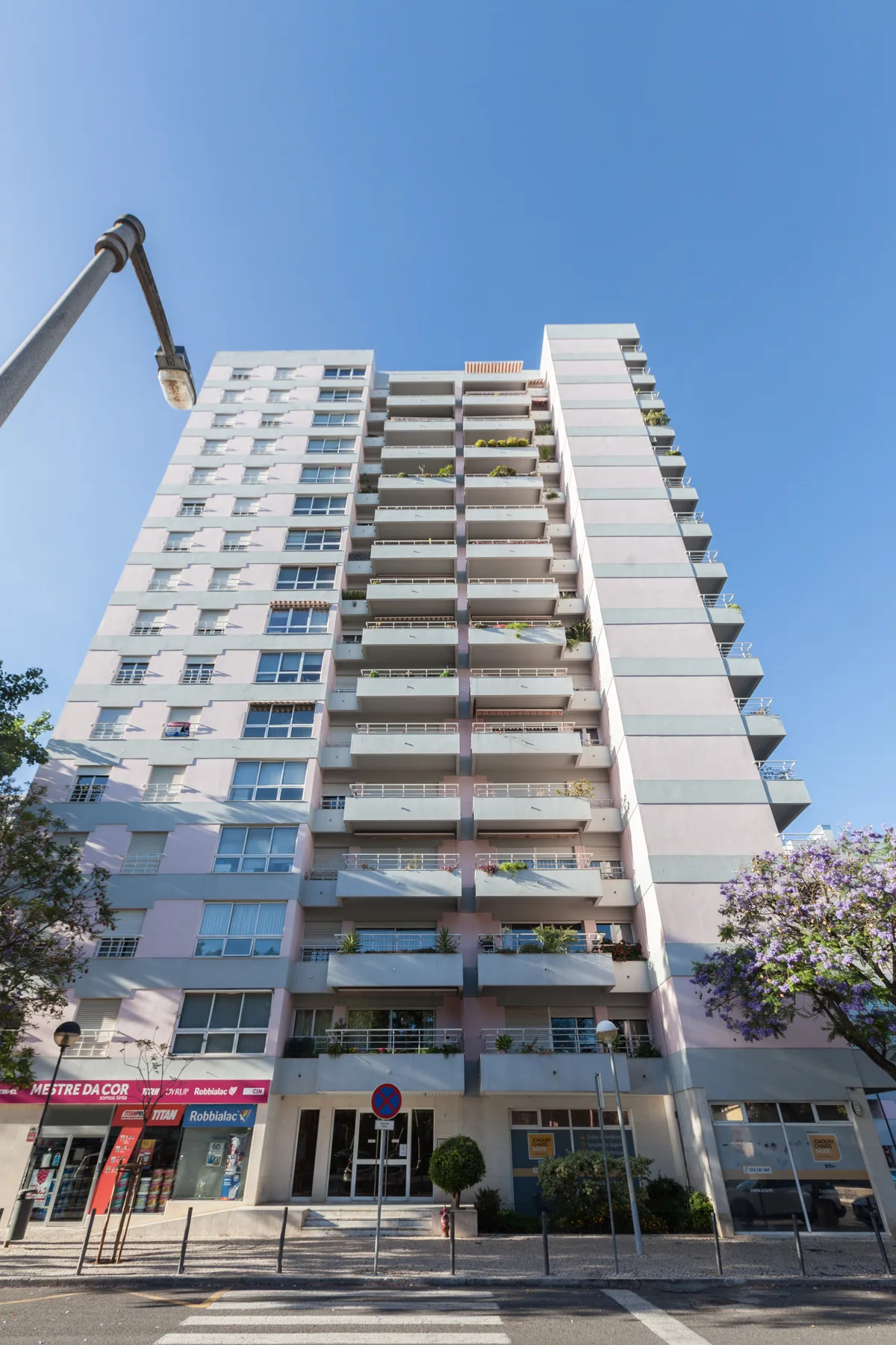 Un edificio alto de apartamentos con balcones y tiendas a nivel de calle bajo un cielo despejado.