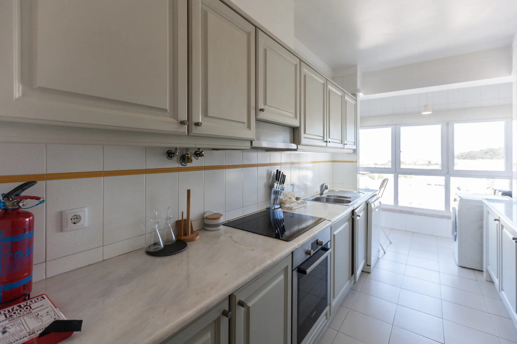 Una cocina luminosa con armarios claros, una encimera y ventanas grandes.