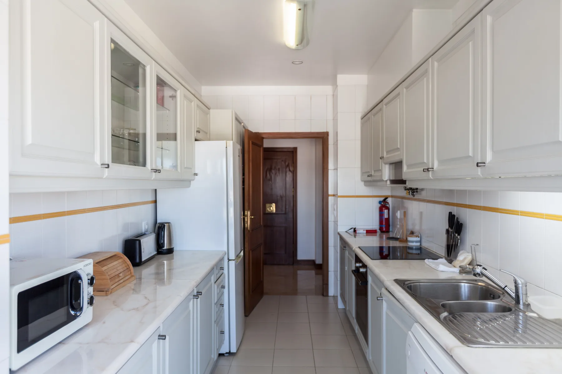 Una cocina estrecha con armarios blancos y encimeras a ambos lados.