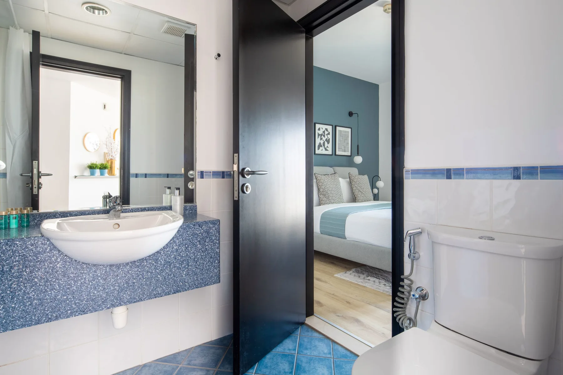 A bathroom vanity and sink sit beside an open doorway to a bedroom.