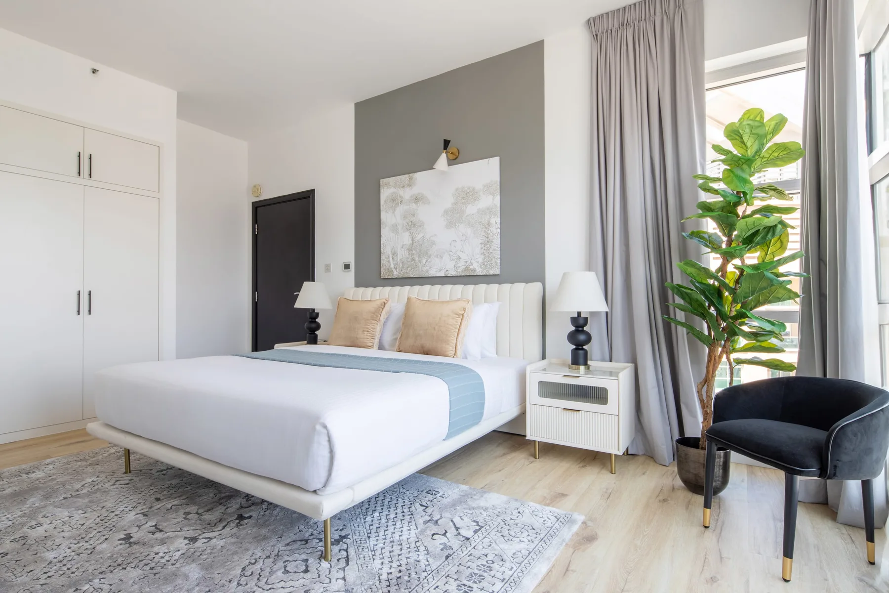 A bright bedroom with a large bed, bedside table, and plant by the window.