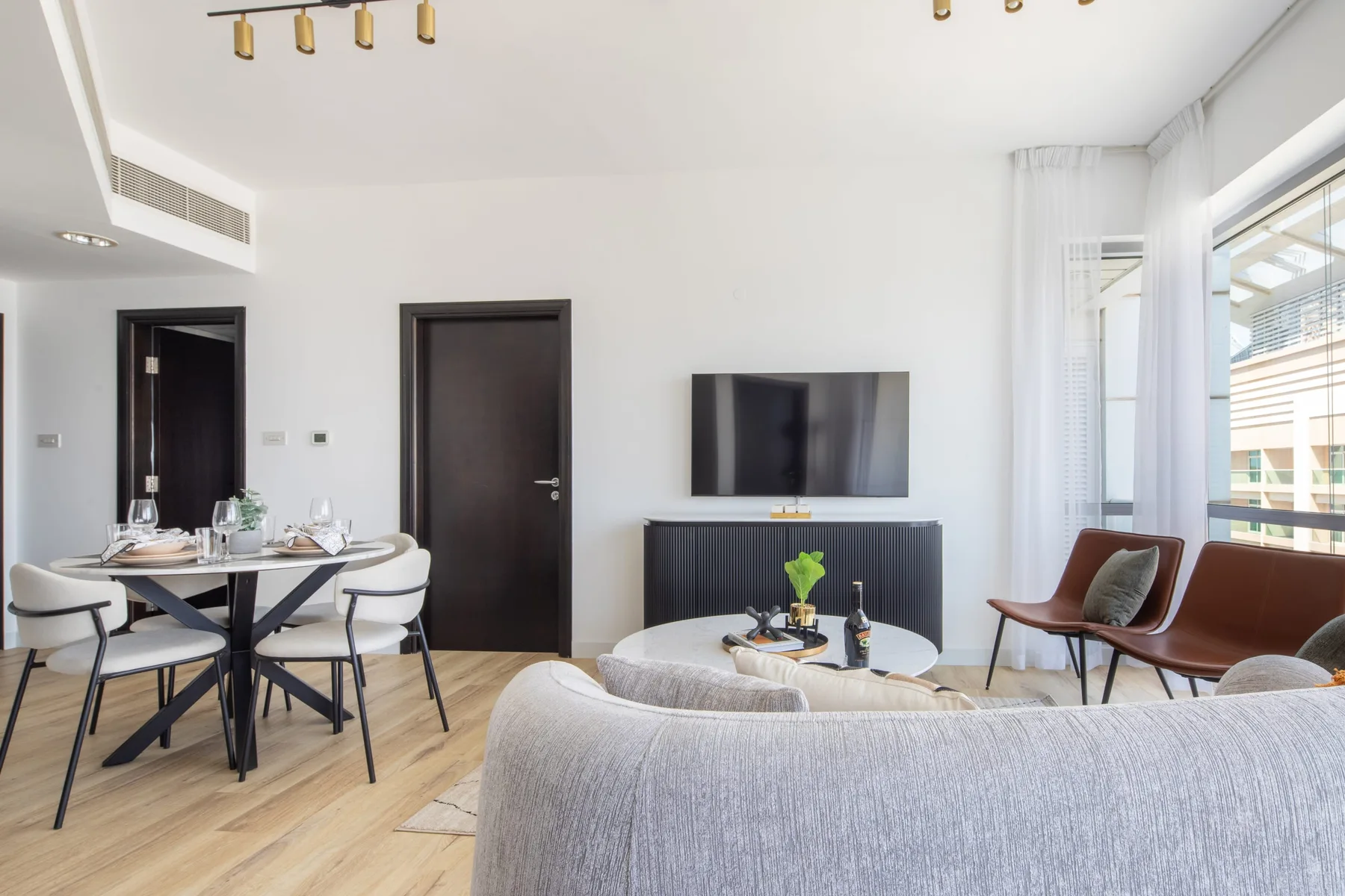 A bright living and dining area with seating, a television, and a table by the windows.