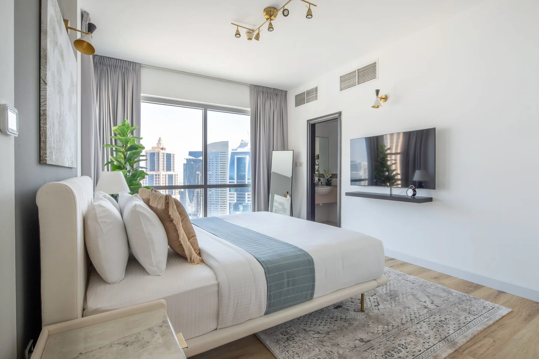 A bright bedroom with a neatly made bed facing a wall-mounted television.