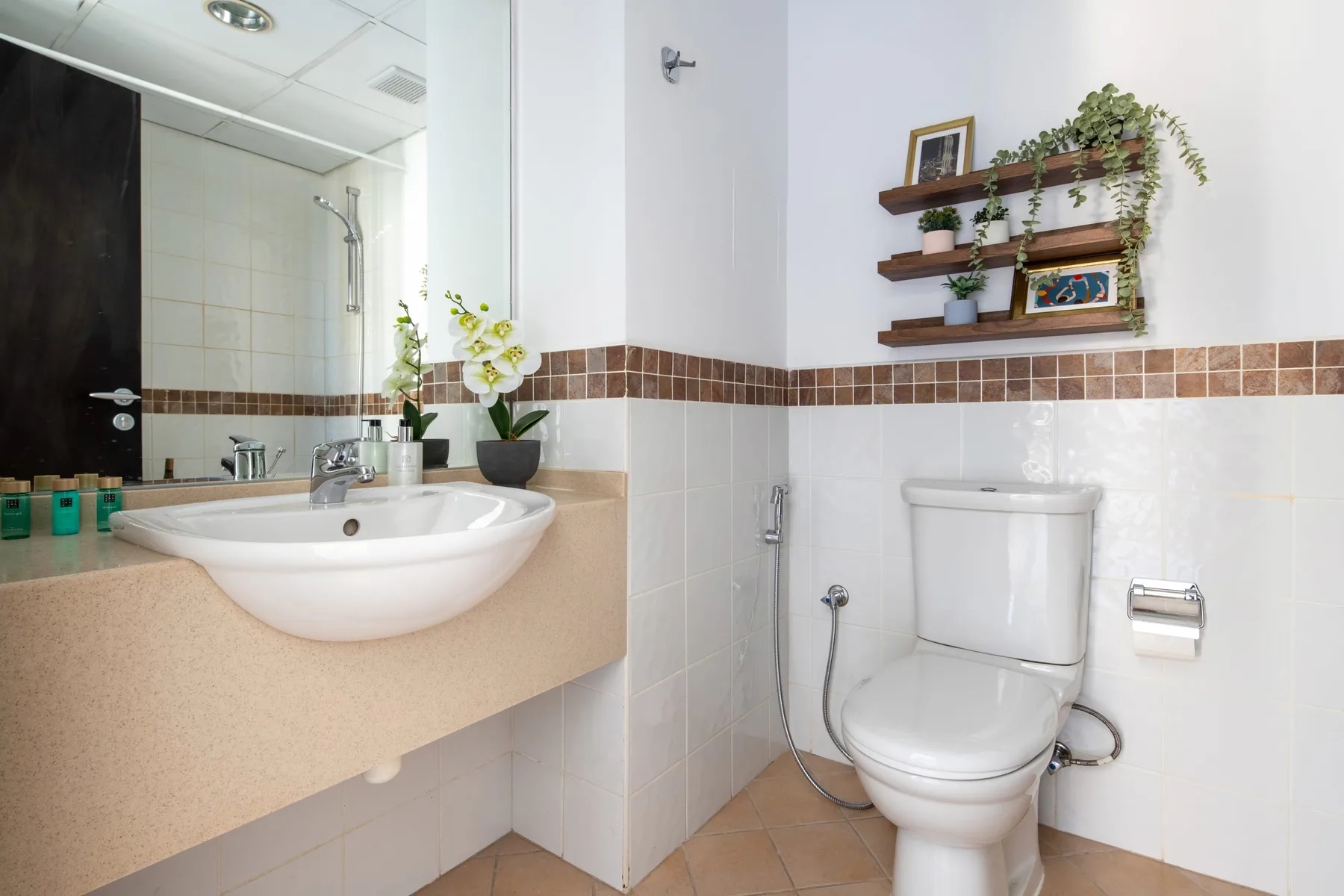 A tiled bathroom with a sink, toilet, and wall-mounted shelves.