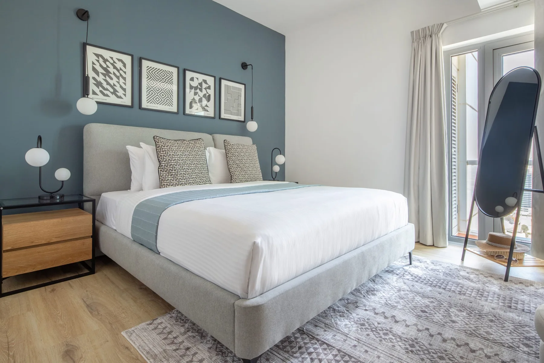 A bedroom with a neatly made bed, framed artwork, and a large window.