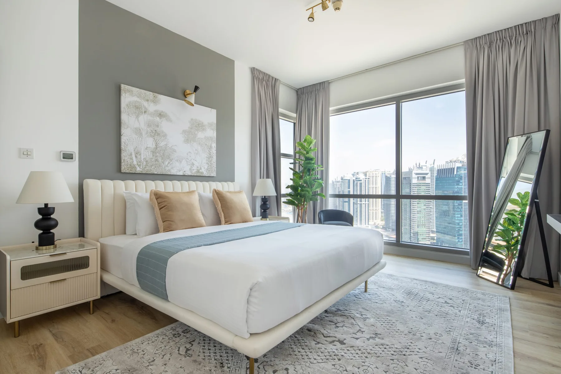 A bright bedroom with a large bed beside floor-to-ceiling windows overlooking the city.