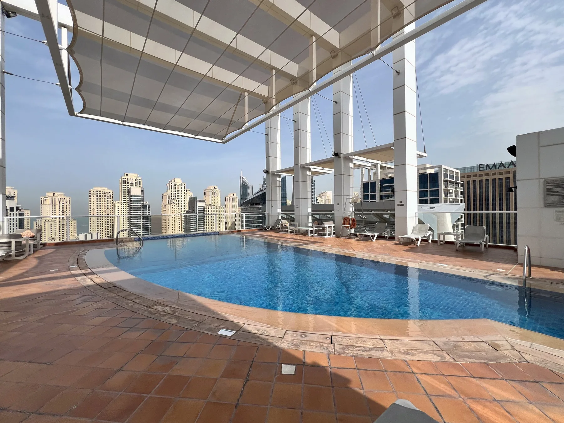 A rooftop swimming pool with surrounding deck seating and city buildings in the background.